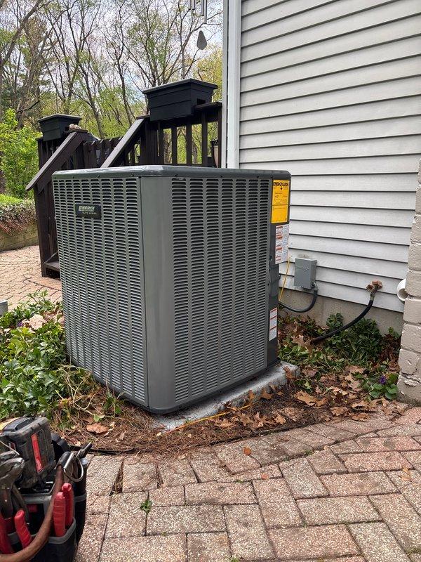 Completed full air conditioning system installation at residential property. Installed new outdoor condensing unit on existing concrete pad adjacent to house exterior, positioned near wooden deck structure. Unit properly mounted with electrical disconnect box and conduit secured to exterior siding. Established refrigerant charge with factory charge of 88 oz and field charge of 6 oz for total system charge of 94 oz. Connected and insulated copper refrigerant lines with service valves installed and capped. Verified all electrical connections, tested system operation, and confirmed proper unit function. Installation site cleaned and unit left operational.