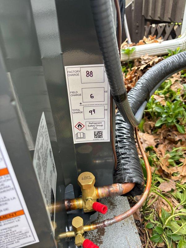Completed full air conditioning system installation at residential property. Installed new outdoor condensing unit on existing concrete pad adjacent to house exterior, positioned near wooden deck structure. Unit properly mounted with electrical disconnect box and conduit secured to exterior siding. Established refrigerant charge with factory charge of 88 oz and field charge of 6 oz for total system charge of 94 oz. Connected and insulated copper refrigerant lines with service valves installed and capped. Verified all electrical connections, tested system operation, and confirmed proper unit function. Installation site cleaned and unit left operational.
