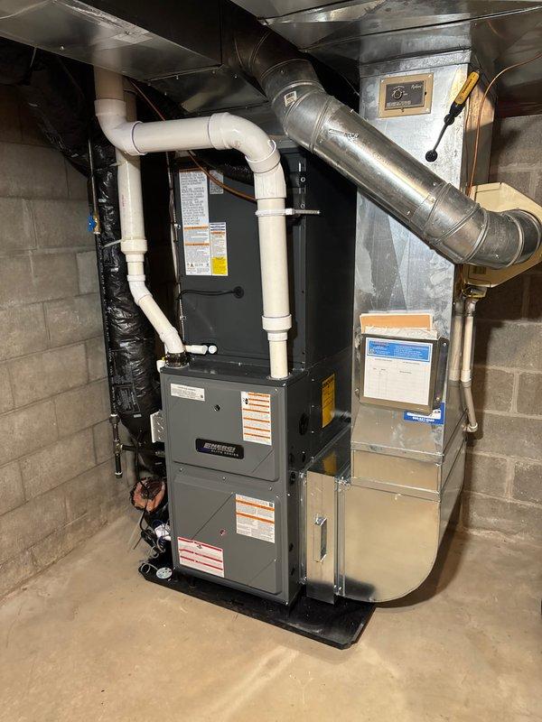 Completed full system replacement including new furnace and air conditioning condenser unit. Installed furnace in basement utility area with proper venting via white PVC piping, mounted on platform base with all ductwork connections secured and integrated with existing distribution system. Positioned new outdoor AC condenser on concrete pad with refrigerant lines and electrical conduit properly routed through exterior wall, junction box mounted, and all connections tested for proper operation.