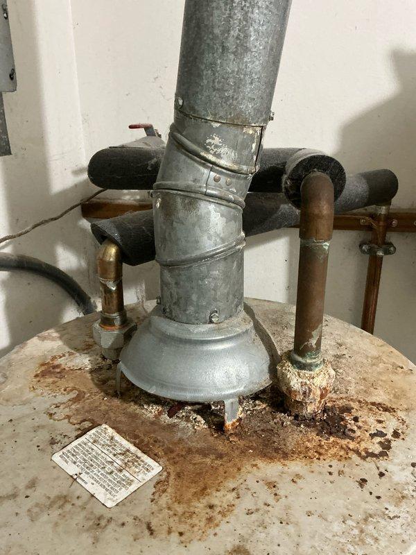Conducted on-site assessment of an eleven-year-old water heater showing significant signs of aging and deterioration. Documented extensive rust corrosion on tank top surface, oxidized copper supply piping with greenish-blue patina, and weathered galvanized exhaust venting system. Provided comprehensive estimate for complete water heater replacement and installation, including removal of existing unit, proper disposal, and installation of new equipment with code-compliant connections and venting.