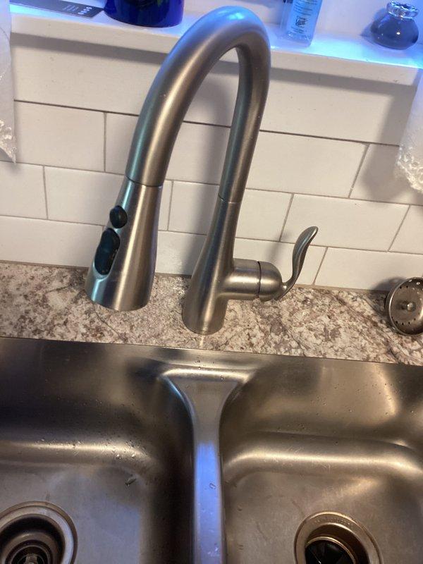 Completed installation of customer-supplied Moen Classic kitchen faucet in approximately 90-year-old residential property. Removed defective faucet that had been causing leak at sink location. Installed new Moen pull-down spray faucet with brushed nickel finish on double-basin stainless steel sink. Connected water supply lines, verified proper operation of pull-down spray head and handle controls, and tested for leaks. New faucet is fully functional with no active leaks detected.