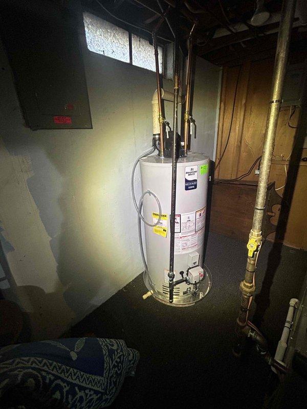 Responded to water leak complaint on 1-year-old Bradford White WT 11-2030 water heater with water discharging from plastic tubing. Upon inspection, identified leak originating from temperature and pressure relief valve discharge pipe. Inspected exterior PVC drainage system and confirmed proper installation of discharge piping through building exterior with appropriate mounting brackets. Verified water heater installation in basement utility room, examined copper supply lines, gas connections with yellow shut-off valve, and overall unit condition. Documented leak source and plumbing configuration for warranty consideration given unit age.