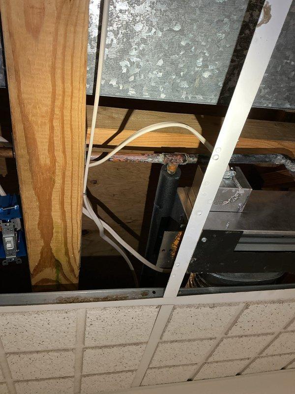 Responded to emergency water leak in guest bedroom ceiling with active steady stream from multiple points. Upon arrival, hot water supply had been shut off by occupant to stop flow. Accessed ceiling cavity through drop ceiling tiles and inspected affected area. Located source of leak in ceiling space above HVAC air handler unit. Documented conditions showing water intrusion around plumbing infrastructure, including PVC piping running through wooden structural framing and joists. Photographed HVAC equipment, ductwork, and surrounding building components to assess extent of water damage and identify leak origin. Inspected metal ductwork, copper refrigerant lines, and ceiling cavity structural members for water damage and compromised integrity. Provided client with documentation of findings and recommendations for necessary repairs to resolve active leak condition.