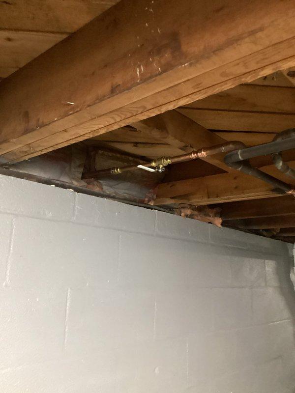 Responded to plumbing leak in basement area. Upon inspection, identified leaking copper pipe with brass fittings in exposed floor joist system above concrete block foundation wall. Documented existing conditions showing moisture staining on wooden joists and structural members, indicating active water intrusion. Assessed plumbing system configuration and determined source of leak requiring repair to prevent further water damage to structural components.