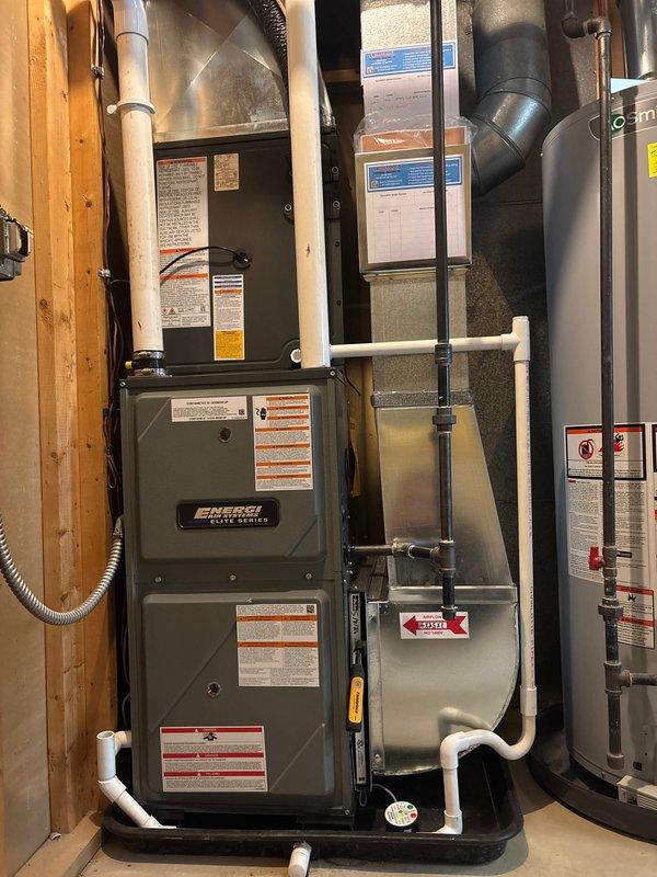 Completed full system replacement of residential HVAC equipment including furnace and air conditioning unit. Installed new Energi Force Center furnace in basement mechanical room with proper condensate drainage via white PVC piping and connected metal supply ductwork. Installed new outdoor AC condenser unit on concrete pad against exterior wall with gray-green finish, positioned electrical disconnect box on wall with conduit connection, and verified proper refrigerant line connections. All equipment tested and operational upon completion, with system ready for service.
