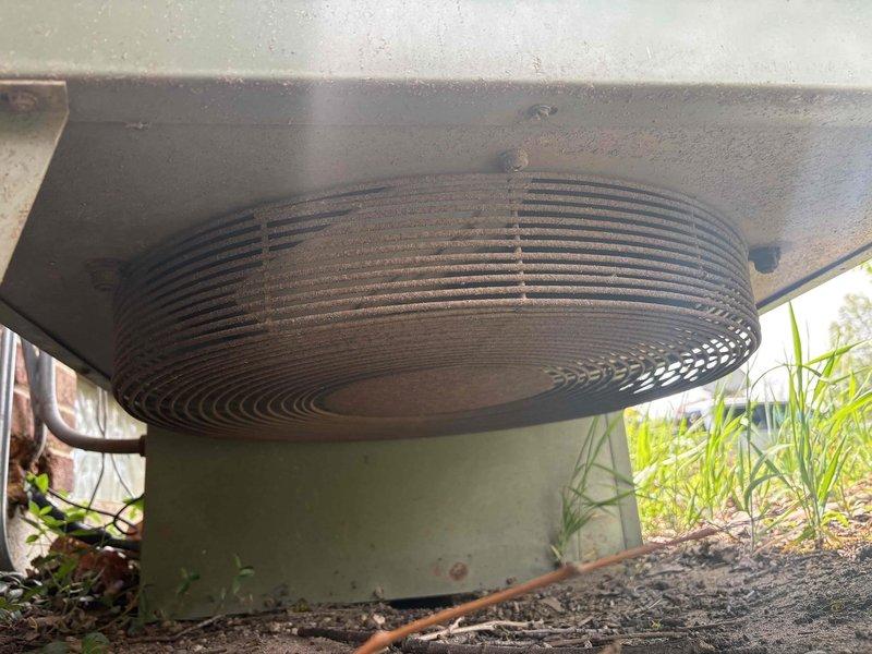 Responded to service call for HVAC system evaluation and relocation estimate. Upon arrival, inspected outdoor condensing unit positioned alongside building exterior. Unit displayed significant accumulation of dirt, dust, and debris on condenser coils and casing, with heavy layer of grime obscuring metal surfaces. Condenser exhibited cylindrical design with spiral coil pattern typical of older equipment configuration. System appeared to be over 10 years in service based on visible wear and weathering patterns.

Conducted thorough visual assessment of unit placement and surrounding area. Equipment currently situated on ground-level pad adjacent to red brick exterior wall with electrical disconnect box and conduit properly mounted. Noted vegetation growth around unit base and debris accumulation on top surface indicating extended exposure to outdoor elements without recent maintenance.

Documented current installation location and condition through photographic evidence for relocation est