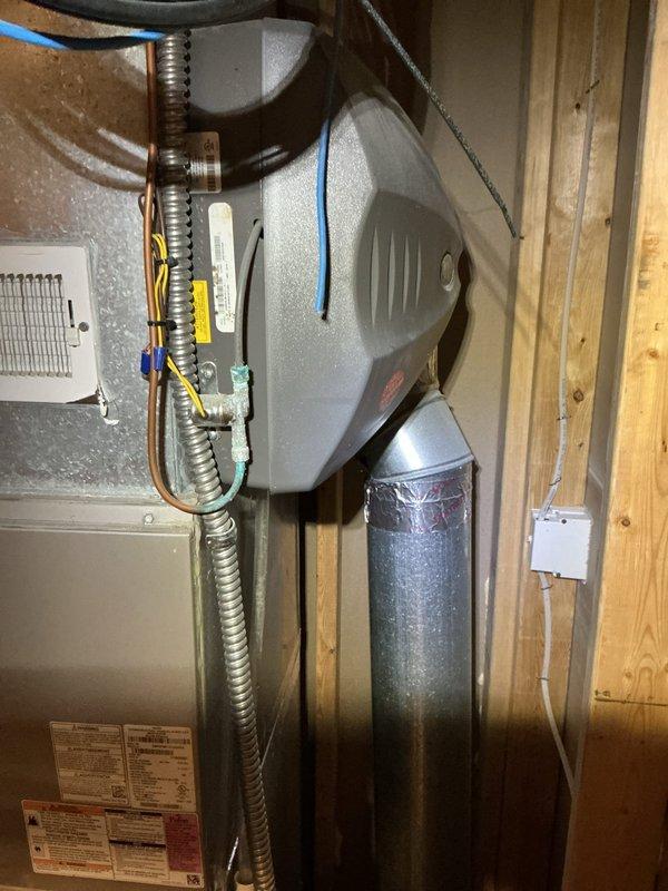 Responded to no cooling complaint on residential HVAC system. Upon arrival, found furnace and humidifier installation in basement utility area with Lochinvar water heater present. Conducted diagnostic evaluation of system blowing room temperature air. Inspected furnace unit, humidifier assembly with vertical metal ductwork, and associated electrical connections including conduit wiring. Verified all mechanical components, plumbing connections, and vent piping configurations. Documented equipment condition and installation setup with photographic records for service file. System age confirmed at less than 10 years old.