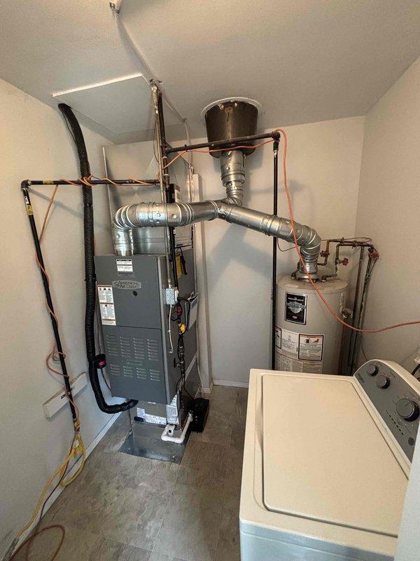 Completed full air conditioning system installation including indoor air handler unit and outdoor condenser unit. Installed new gray furnace/air handler in interior utility room with proper refrigerant line connections, electrical conduit, and flexible ductwork routing. Mounted outdoor condenser unit on pad adjacent to building exterior with electrical whip connection secured to siding. Verified all refrigerant lines, electrical connections, and condensate drainage properly installed and operational. System tested and confirmed cooling operation.