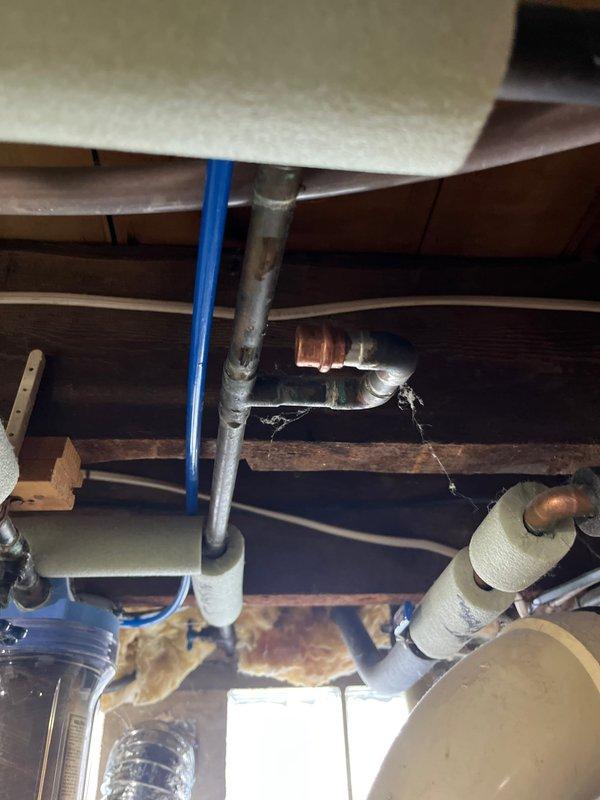 Responded to plumbing leak in basement. Upon inspection, identified active leak at copper pipe connection point beneath flooring structure. Found deteriorated tape wrap and corroded copper piping showing green oxidation and water damage to surrounding wooden joists and subfloor. Removed failed valve assembly and damaged fittings. Cut out compromised section of copper pipe using pipe cutter. Installed new chrome-plated valve fitting with proper threaded connections. Secured all joints and tested system for proper water flow and pressure. Verified no additional leaks present. Cleaned work area and removed debris.