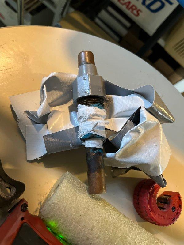 Responded to plumbing leak in basement. Upon inspection, identified active leak at copper pipe connection point beneath flooring structure. Found deteriorated tape wrap and corroded copper piping showing green oxidation and water damage to surrounding wooden joists and subfloor. Removed failed valve assembly and damaged fittings. Cut out compromised section of copper pipe using pipe cutter. Installed new chrome-plated valve fitting with proper threaded connections. Secured all joints and tested system for proper water flow and pressure. Verified no additional leaks present. Cleaned work area and removed debris.