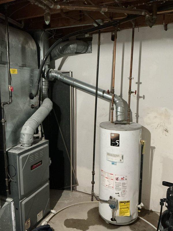 Responded to service call for leaking water heater in basement utility room. Upon inspection, identified active leak originating from water heater tank connections. Assessed copper piping, isolation valves, and mounting configuration. Documented existing conditions including moisture damage and wall discoloration behind unit, indicating prolonged leak exposure. Captured photographic evidence of mechanical room layout, HVAC equipment proximity, and water heater installation for service records. Recommended water heater replacement due to age and extent of deterioration observed at connection points and tank integrity concerns.