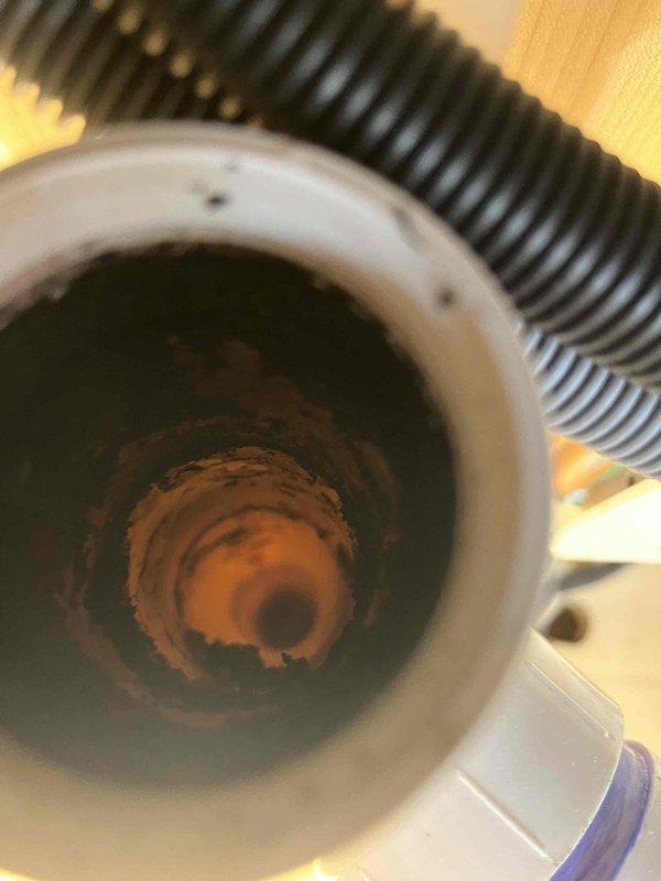 Responded to kitchen drain leak. Upon inspection, discovered severe corrosion and rust accumulation inside the drain tailpiece assembly beneath the sink. The white PVC drain components showed significant deterioration with heavy brownish-orange rust deposits forming concentric patterns throughout the interior of the pipe, indicating prolonged water damage and compromised integrity of the drainage system. Documented the corroded condition with photographs showing the extent of buildup within the cylindrical drain component. Assessed the complete under-sink plumbing configuration, including the P-trap assembly, garbage disposal connections, flexible drainage hoses, and associated PVC fittings. The corrosion level required replacement to prevent future leaks and ensure proper drainage function. Completed necessary repairs to restore the kitchen drain system to proper working condition.