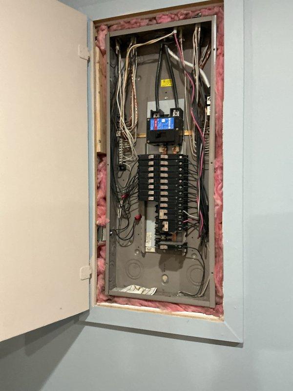 Completed comprehensive electrical club inspection of main service panel. Documented current panel configuration showing dual-column circuit breaker arrangement with main disconnect, integrated surge protection device, and multiple branch circuits. Observed exposed insulation around panel perimeter where drywall opening extends beyond panel frame. Captured detailed photographs of panel interior showing wire routing, breaker layout, and overall system condition for maintenance records and future reference.