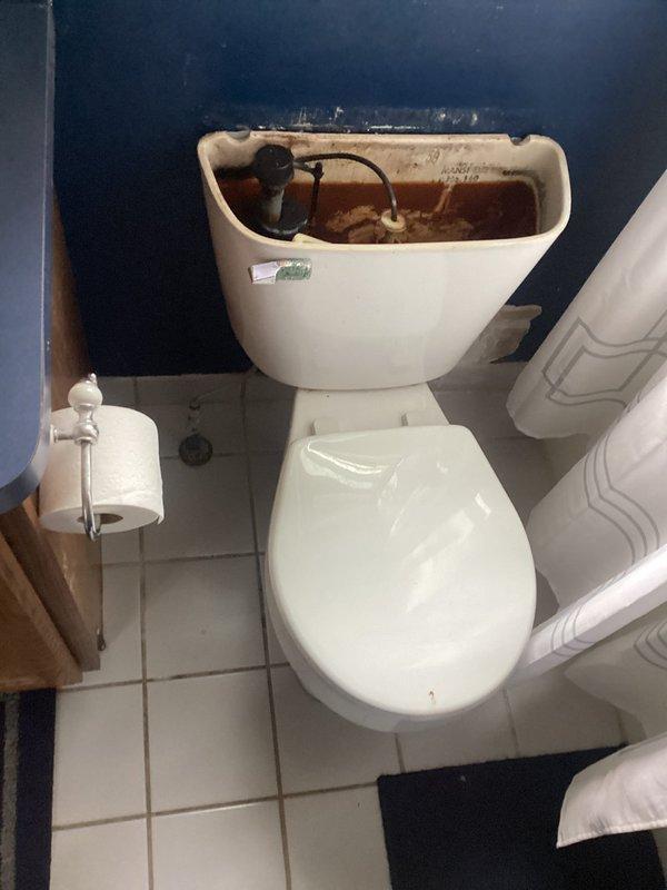 Responded to toilet tank not holding water. Upon inspection, found deteriorated internal flush mechanism components with significant rust and mineral deposits throughout tank interior. Removed tank lid and assessed fill valve, flush valve, and float assembly. Identified failed flapper valve as primary cause of continuous water loss. Replaced worn flapper and inspected tank-to-bowl seal for integrity. Noted evidence of long-term water damage on adjacent bathroom wall and floor, including visible staining and deterioration. Tested flush cycle and verified proper water retention after repairs. System restored to normal operation.