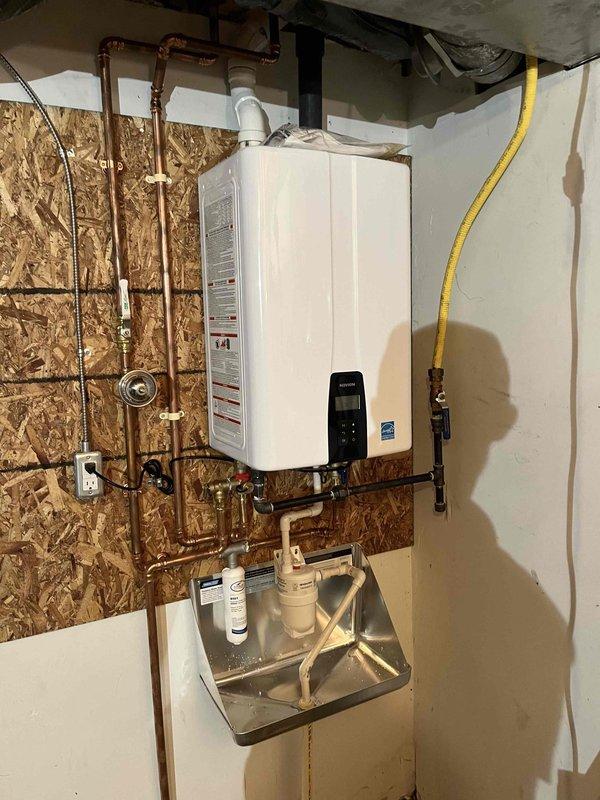 Successfully installed a Navien NPE-210A2 natural gas tankless water heater system in utility room. Mounted unit to OSB wall with proper support, connected copper supply lines with brass shut-off valves and fittings, and installed metal drip pan with dual water filter housings for system protection. Ran white PVC venting from unit exhaust, installed yellow flexible gas line with brass shut-off valve for fuel supply, and verified all electrical connections to digital control panel. Tested all plumbing connections for leaks, confirmed proper gas flow and combustion, programmed unit settings, and verified hot water delivery throughout the system.