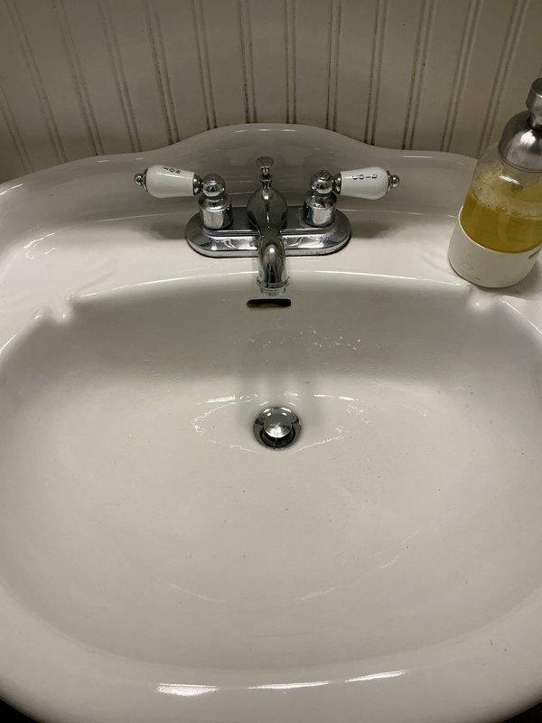 Responded to main bathroom for leaking faucet repair. Upon inspection, identified leak at traditional two-handle chrome faucet with porcelain handle inserts on white oval sink. Disassembled faucet handles, replaced worn cartridges and seals, reassembled unit, and tested both hot and cold water lines to confirm leak was eliminated and proper operation restored.