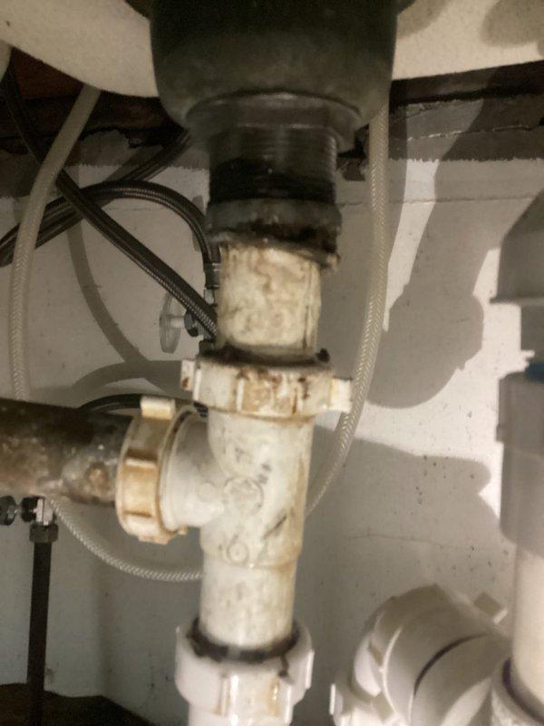 # Kitchen Sink Leak Repair

Responded to intermittent water leak under kitchen sink in century-old home. Upon inspection, discovered deteriorated PVC P-trap assembly with significant age-related degradation, including discoloration, staining, and compromised seals at slip joint connections beneath garbage disposal. White PVC drain components showed extensive wear patterns and brown staining concentrated around connection points, indicating long-term water seepage. 

Identified failing compression rings and worn slip joint gaskets as primary leak sources. P-trap configuration exhibited loose fittings and degraded washers allowing water to escape during drainage cycles, explaining the intermittent nature of the leak. Braided supply lines and shutoff valves inspected and found to be functioning properly with no evidence of supply-side leakage.

Disassembled existing P-trap assembly and removed all deteriorated components. Cleaned mounting surfaces and disposal tailpiece to ensure proper s
