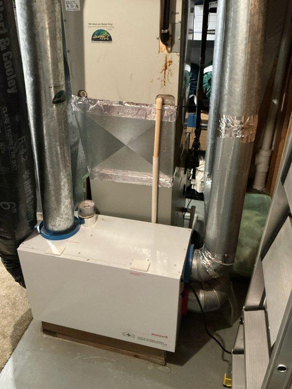 Completed sales estimate for aging residential HVAC system installed in basement utility room. Documented existing air handler unit with associated ductwork, including vertical metal supply ducts with foil-taped connections, flexible ductwork, and refrigerant lines. System shows significant age with visible wear on components and ductwork connections. Photographed current installation configuration including plenum assembly, copper refrigerant piping, and mechanical room layout to provide comprehensive assessment for equipment replacement recommendations.