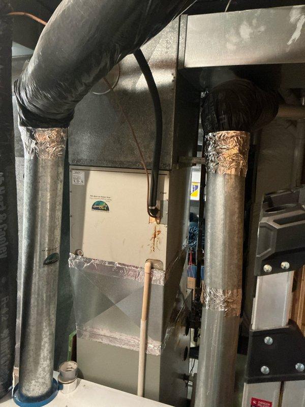 Completed sales estimate for aging residential HVAC system installed in basement utility room. Documented existing air handler unit with associated ductwork, including vertical metal supply ducts with foil-taped connections, flexible ductwork, and refrigerant lines. System shows significant age with visible wear on components and ductwork connections. Photographed current installation configuration including plenum assembly, copper refrigerant piping, and mechanical room layout to provide comprehensive assessment for equipment replacement recommendations.