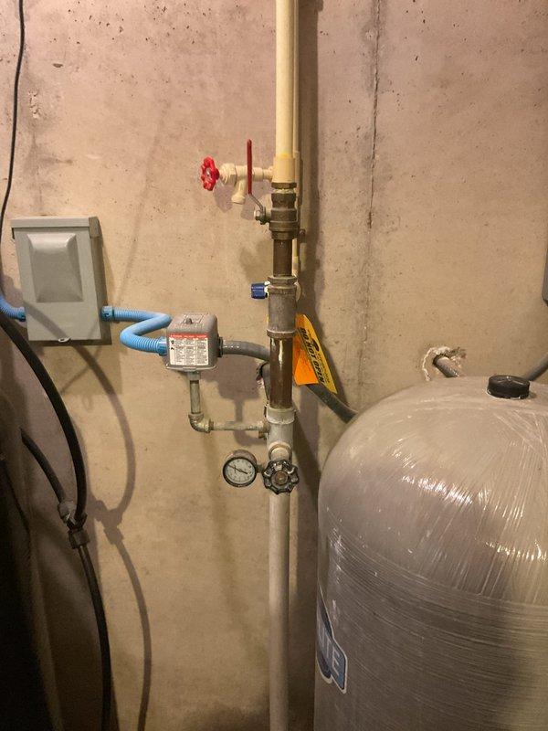 Conducted on-site assessment of existing well pressure tank system for estimate revision. Documented current installation including pressure tank with associated piping, valves, pressure gauge, and control components. Photographed complete system setup showing tank mounted on base, PVC supply lines with shutoff valves, pressure switch assembly, and connections to water distribution system. Verified all equipment specifications and configuration details necessary for preparing updated estimate documentation.