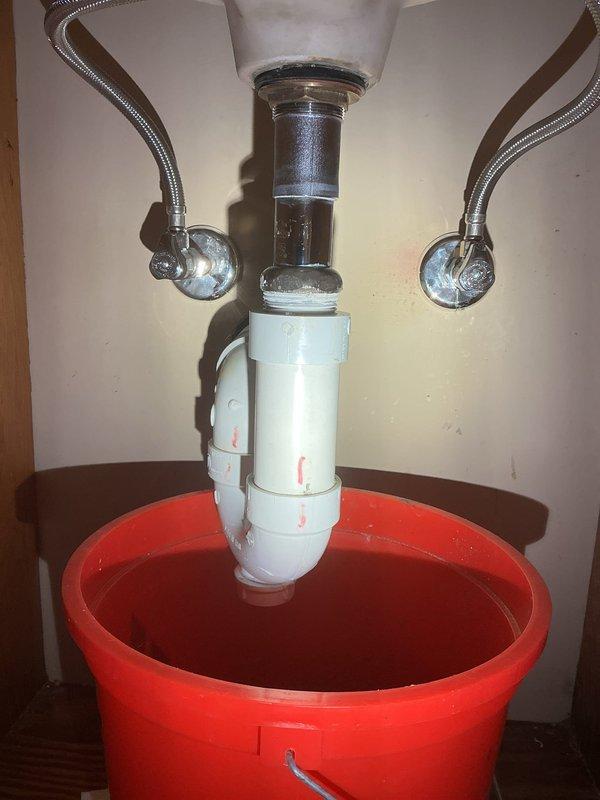 Responded to a callback for a leaking bathroom sink drain that was recently serviced. Upon arrival, inspected the P-trap assembly and slip joint connections beneath the sink. Identified loose connection at the P-trap causing water to drip into the bucket positioned below. Tightened slip joint nuts on the white PVC P-trap assembly and verified proper seal at both the tailpiece connection and drain outlet. Tested the drain system by running water through the fixture and confirmed no leaks present at any connections. Removed bucket and left plumbing system in proper working order.