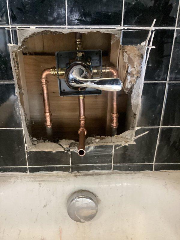 Responded to upstairs bathtub faucet with persistent hot water drip that had worsened over several months. Upon inspection, found original plumbing fixtures in 1910-era home with worn internal valve components causing constant leak and requiring excessive force to operate handles. Accessed valve assembly through black tile wall to evaluate copper supply lines and mixing valve condition. Replaced faulty cartridge and internal seals in chrome shower valve assembly. Addressed tight knob operation by servicing valve stems and lubricating moving components. Tested hot and cold water lines for proper flow and pressure balance. Verified complete elimination of drip after repairs and confirmed smooth handle operation. Restored fixture to full functionality, allowing normal tub use to resume.