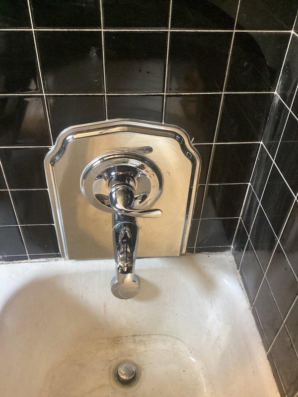 Responded to upstairs bathtub faucet with persistent hot water drip that had worsened over several months. Upon inspection, found original plumbing fixtures in 1910-era home with worn internal valve components causing constant leak and requiring excessive force to operate handles. Accessed valve assembly through black tile wall to evaluate copper supply lines and mixing valve condition. Replaced faulty cartridge and internal seals in chrome shower valve assembly. Addressed tight knob operation by servicing valve stems and lubricating moving components. Tested hot and cold water lines for proper flow and pressure balance. Verified complete elimination of drip after repairs and confirmed smooth handle operation. Restored fixture to full functionality, allowing normal tub use to resume.
