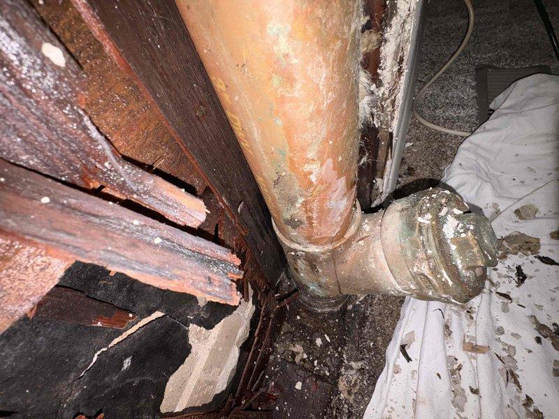 Responded to emergency plumbing leak from main toilet cleanout causing water infiltration into basement. Upon arrival, found severely corroded copper piping with failed connection at cleanout fitting, resulting in active water discharge and extensive ceiling and wall damage to lower level. Documented deteriorated plumbing infrastructure showing heavy rust, mineral deposits, and compromised brass fittings. Evidence of prolonged moisture exposure included damaged wooden structural members, ceiling material removal exposing joists and piping, and significant water staining throughout affected area. Photographed corroded pipe sections, failed connections, and resulting structural damage for documentation purposes.