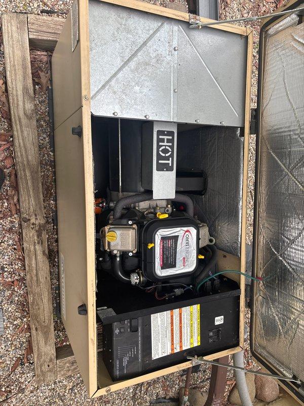 Responded to service call for 20-year-old Generac generator that failed to start during recent power outage and was not executing weekly self-test cycles. Upon arrival, performed comprehensive diagnostic evaluation of unit housed in ventilated wooden enclosure. Inspected engine compartment, checking fluid levels including oil reservoir identified by yellow dipstick cap. Examined air intake system with corrugated rubber hose and clamp connections for proper sealing and debris obstruction. Verified battery connections and charging system functionality. Tested control board operations and self-test programming parameters. Cleaned accumulated dirt, dust, and debris from engine bay and critical components affecting proper ventilation and operation. Documented equipment condition through photographic records showing engine compartment details and overall unit configuration with protective metal hood and warning labels. Restored generator to operational status with confirmed successful start 