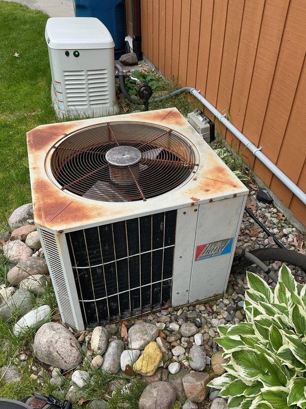 Completed annual cooling system tune-up and inspection on 37-year-old outdoor air conditioning condenser unit. Performed comprehensive maintenance protocol including visual inspection, coil cleaning, electrical connections check, refrigerant level assessment, and operational testing. Unit shows significant age-related weathering with extensive rust discoloration on top panel surfaces, though system remains functional. Verified proper operation of condenser fan motor, compressor function, and overall cooling performance. Documented equipment condition with photographic evidence showing installation alongside standby generator unit with proper clearances maintained. All electrical connections at exterior panel and meter box verified secure. System operating within acceptable parameters at time of service completion.