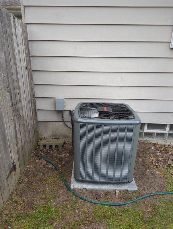 Completed full HVAC system installation including new furnace and air conditioning condenser unit. Installed outdoor AC unit on concrete pad against exterior wall with proper electrical conduit connection and positioned unit between house and fence line. Installed high-efficiency furnace in basement utility area with associated white PVC condensate drain lines and venting components. Connected metal ductwork with insulated flexible ducting transitions. Verified all mechanical connections, electrical hookups, and proper system operation upon completion.