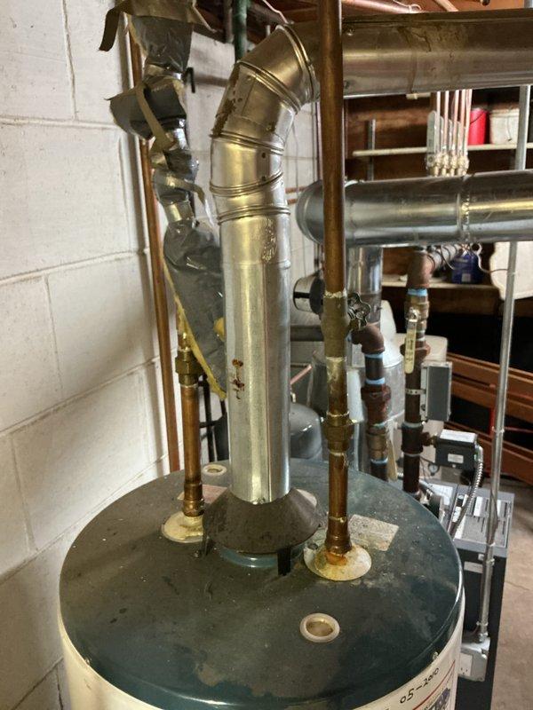 Conducted site assessment for replacement of 15-year-old 40-gallon residential water heater located in basement utility area. Evaluated existing installation including copper supply piping, brass connections, metallic flue vent system with elbow joint, and current configuration within concrete block utility room. Documented current system condition showing age-related wear on tank surfaces and verified standard residential installation requirements for proper replacement specifications. Photographed existing plumbing infrastructure, insulated copper lines, galvanized ductwork, and surrounding mechanical components to prepare accurate replacement estimate for new water heater installation.