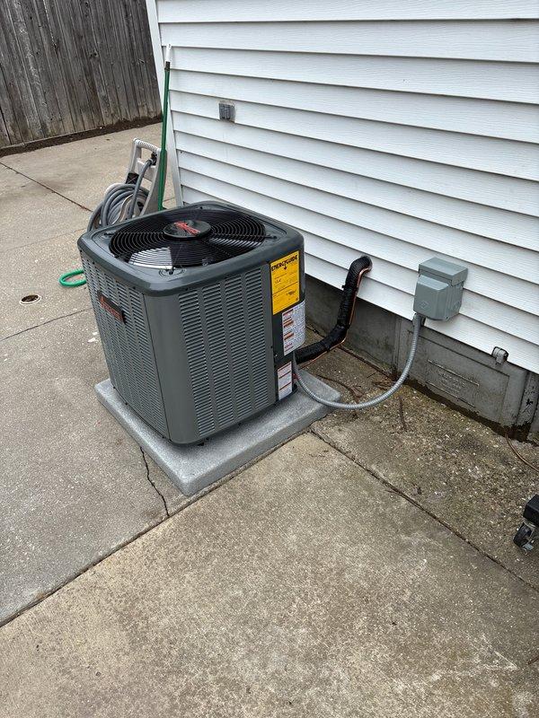 Completed full air conditioning system replacement at residential property. Removed existing outdoor condenser unit and installed new dark gray condensing unit on existing concrete pad against house exterior with proper clearances. Connected refrigerant lines through exterior wall penetration, installed electrical disconnect box, and completed all line set insulation and weatherproofing. System was charged, tested, and verified operational with all manufacturer specifications met.