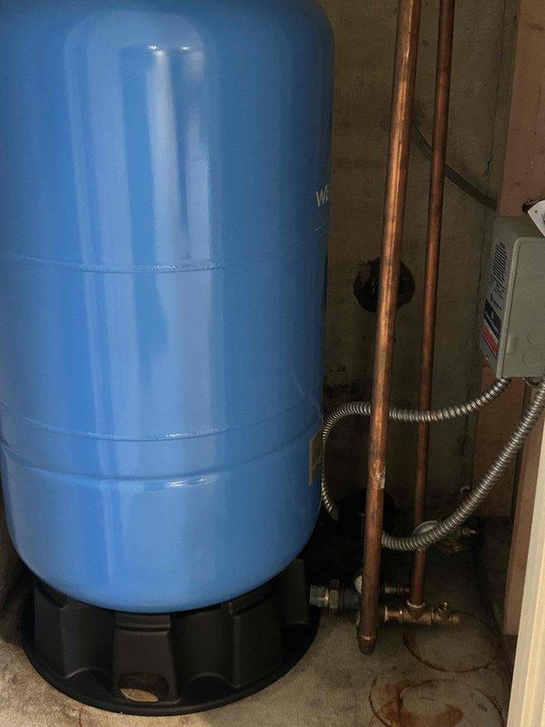 Replaced residential well pressure tank system. Installed new blue pressure tank with proper plumbing connections including copper piping and flexible conduit. Verified system operation and confirmed proper air pressure at 38.0 PSI using digital gauge at tank valve.
