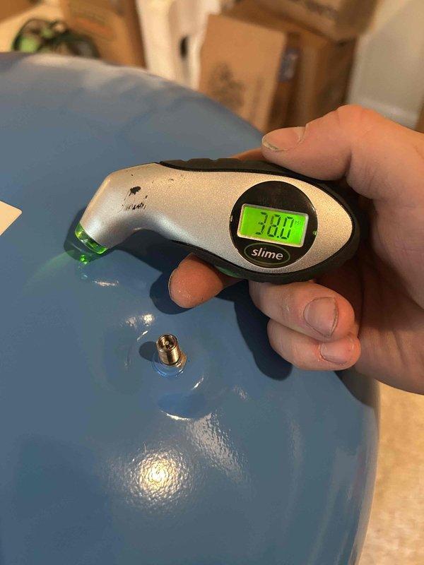 Replaced residential well pressure tank system. Installed new blue pressure tank with proper plumbing connections including copper piping and flexible conduit. Verified system operation and confirmed proper air pressure at 38.0 PSI using digital gauge at tank valve.