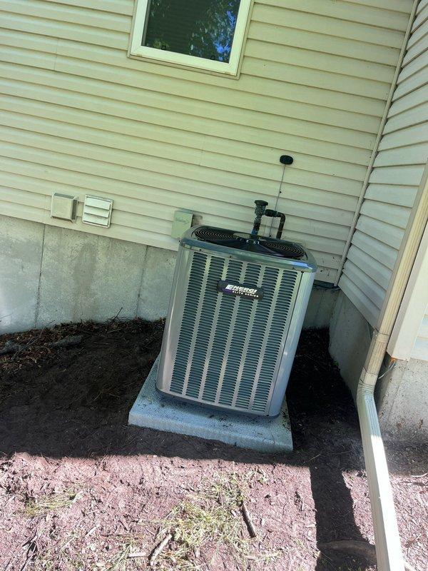 Completed full HVAC system replacement including outdoor condensing unit and indoor air handler/furnace assembly. Installed new condenser on existing concrete pad against exterior wall with proper clearances maintained. Mounted unit features horizontal louver grille design with manufacturer specifications clearly labeled. Interior installation includes new furnace unit with dual vertical metallic supply and return ductwork, properly insulated with reflective foil wrap and secured with metallic tape. Connected black flexible insulated ductwork to distribution system. Installed condensate drain pan at base of unit. Verified all copper refrigerant lines properly connected and insulated. Ensured electrical connections secure at outdoor unit. System tested and operating within manufacturer specifications.