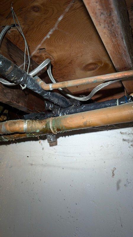 # AC Annual Cooling Maintenance - 16-Year-Old System

Completed comprehensive annual cooling maintenance on a 16-year-old air conditioning system. Upon arrival, discovered significant water accumulation on basement floor near HVAC equipment area, with moisture present around utility room perimeter and door frame base. Flexible drainage hose was positioned on floor, indicating recent water management efforts.

Inspected overhead plumbing and refrigerant line infrastructure in basement ceiling area. Examined copper refrigerant lines showing age-appropriate patina and verified integrity of all pipe joints and connections. Assessed flexible refrigerant line insulation and securing points, noting dark tape wrapping at multiple locations along the line set. Confirmed proper mounting and support of all overhead mechanical systems against floor joists.

Performed standard AC tune-up procedures including system performance evaluation, refrigerant pressure checks, and operational testing of all 