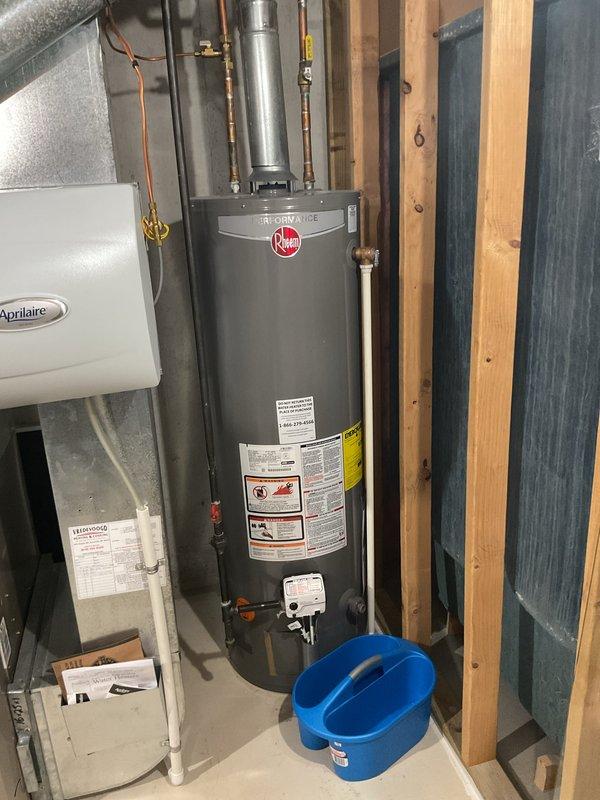 Responded to water heater leak on 4-year-old Rheem ProMaxx unit. Upon inspection, identified active leak at base of water heater with visible rust and corrosion on lower components. Placed bucket to contain leaking water while customer maintained hot water availability. Documented equipment condition with photographs showing water damage and oxidation at leak point. Advised customer of findings and recommended replacement due to extent of corrosion on tank base.
