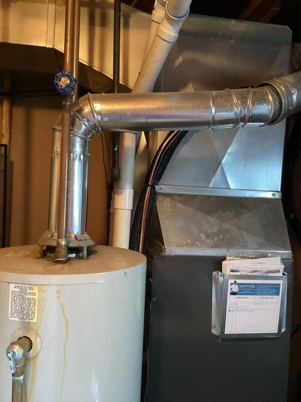 Responded to service call for leaking water heater over 20 years old. Upon arrival, inspected residential water heater located in basement utility area adjacent to furnace system. Identified active leak at plumbing connections and assessed overall condition of unit. Documented equipment age and deterioration through photographic documentation showing water heater installation, surrounding HVAC equipment, and mechanical room configuration. Due to advanced age of unit exceeding typical service life expectancy, recommended replacement rather than repair. Customer opted for cash/check without warranty coverage.