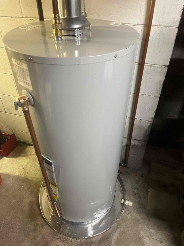 Successfully completed water heater installation in basement utility area. Removed existing unit and installed new white cylindrical water heater on concrete floor with proper metallic base plate. Connected copper supply lines with brass compression fittings and installed metallic vent pipe at top of unit with secure brass fittings. Verified all plumbing connections for proper seal and tested unit for leaks. Ensured compliance with manufacturer specifications and local code requirements. Unit tested and operational upon completion.