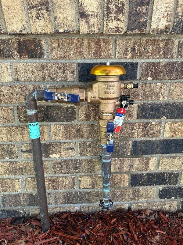 Responded to service call for two plumbing issues: exterior vacuum breaker leaking at irrigation system backflow preventer and noisy downstairs bathtub faucet when operated at certain temperatures. Inspected exterior sprinkler system vacuum breaker assembly mounted on brick wall, which had been leaking since previous spring season. Evaluated backflow prevention device, pressure relief valve, and associated piping connections for signs of failure or deterioration. Examined downstairs bathtub fixture including spout, diverter control, and faucet assembly on tiled wall for source of temperature-related noise issue that had persisted since installation. Documented condition of both fixtures with photographs showing weathered exterior plumbing components with surface corrosion and aged bathroom hardware with water staining. Provided assessment and recommendations for repair or replacement of affected components to resolve ongoing leak and noise concerns at both isolated fixture locations.