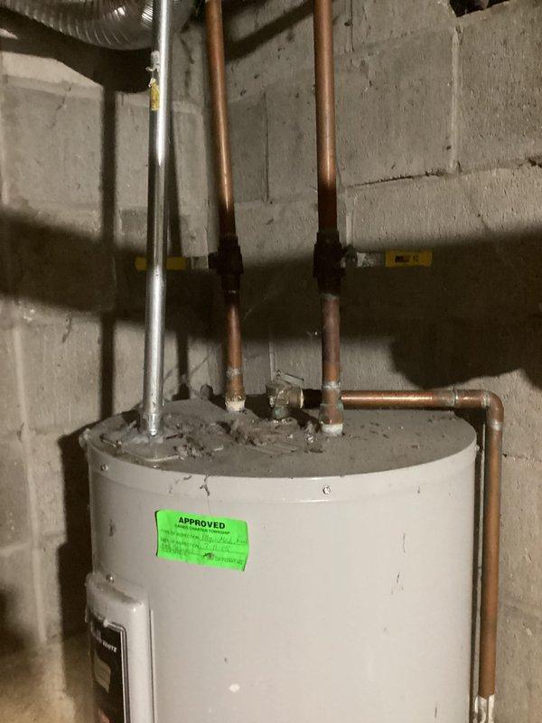 Provided estimate for replacement of existing residential water heater located in basement utility area. Unit assessed is an aging white cylindrical tank-style water heater with standard copper and metal pipe connections at top, showing visible dirt accumulation and wear consistent with extended service life. Documented current installation configuration including hot and cold water supply lines, electrical connections via wall-mounted conduit box, and proper venting system with PVC drainage components for customer's consideration of replacement options.