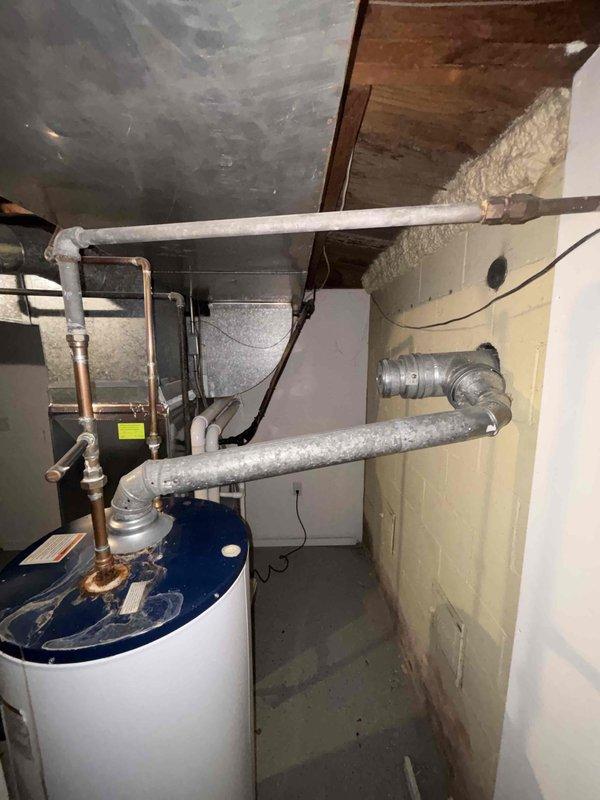 Provided estimate for replacement of existing 40-gallon natural gas water heater in single family residence. Unit located in basement utility area with existing copper supply lines, brass shut-off valves, and proper venting infrastructure already in place. Documented current installation including water heater positioning, plumbing connections, and surrounding mechanical systems for accurate replacement specifications.