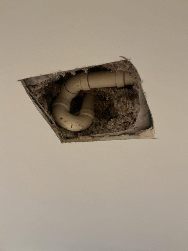 Responded to water leak service call where homeowner accidentally drilled into plumbing pipe during home improvement work. Accessed affected area through ceiling, identified damaged PVC drain pipe in P-trap configuration, and documented condition showing water damage and debris accumulation around penetration point. Created access opening in ceiling to expose plumbing system for assessment and repair preparation.