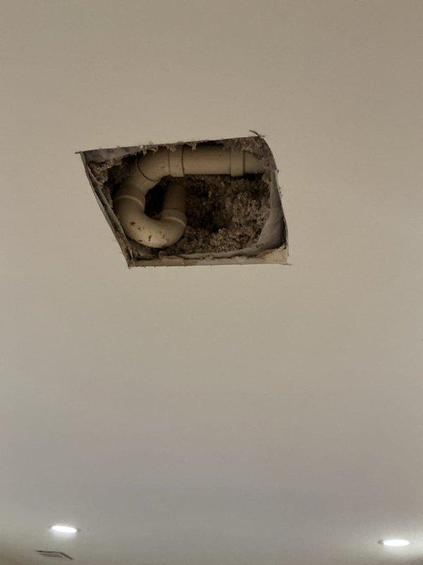 Responded to water leak service call where homeowner accidentally drilled into plumbing pipe during home improvement work. Accessed affected area through ceiling, identified damaged PVC drain pipe in P-trap configuration, and documented condition showing water damage and debris accumulation around penetration point. Created access opening in ceiling to expose plumbing system for assessment and repair preparation.