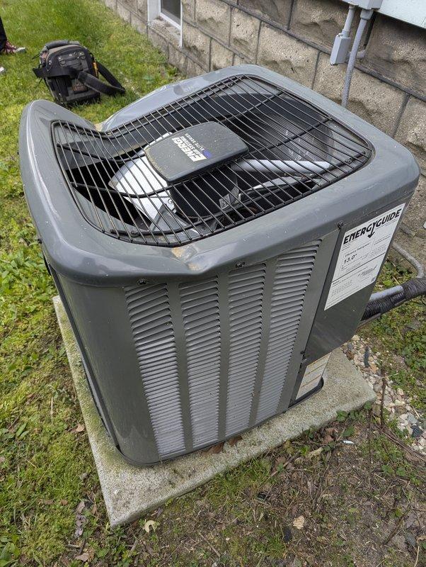 Responded to no cooling complaint on 4-year-old EnergiAir system. Upon arrival, discovered damaged condenser top grille with corner section broken and detached, creating an opening in the unit housing. Inspected outdoor condenser unit positioned on concrete pad against building exterior, noting the compromised fan guard assembly that could allow debris entry and posed potential safety concerns. Documented equipment condition with photographs showing the separated grille cover and overall unit status. Unit exterior showed normal weathering for age with no additional significant damage observed to cabinet or ventilation louvers.