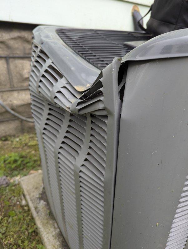 Responded to no cooling complaint on 4-year-old EnergiAir system. Upon arrival, discovered damaged condenser top grille with corner section broken and detached, creating an opening in the unit housing. Inspected outdoor condenser unit positioned on concrete pad against building exterior, noting the compromised fan guard assembly that could allow debris entry and posed potential safety concerns. Documented equipment condition with photographs showing the separated grille cover and overall unit status. Unit exterior showed normal weathering for age with no additional significant damage observed to cabinet or ventilation louvers.