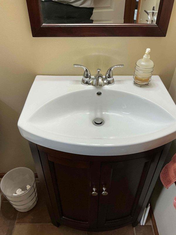 Installed chrome two-handle centerset faucet on bathroom vanity with white ceramic sink basin. Faucet was properly mounted, supply lines connected, and system tested to ensure proper water flow and no leaks.