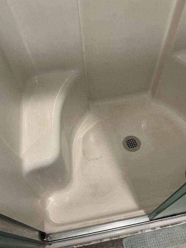 Responded to plumbing leak complaint originating from master bathroom shower causing water intrusion into flooring below. Conducted thorough inspection of shower stall, including white fiberglass enclosure, drain assembly, and surrounding components. Documented existing conditions with photographs showing shower pan configuration, built-in seating ledge, center drain with metal grid cover, and glass door assembly with chrome framing. Identified potential leak sources and assessed shower base integrity, wall sealing, and drain connections to determine cause of water migration into subfloor during shower operation.