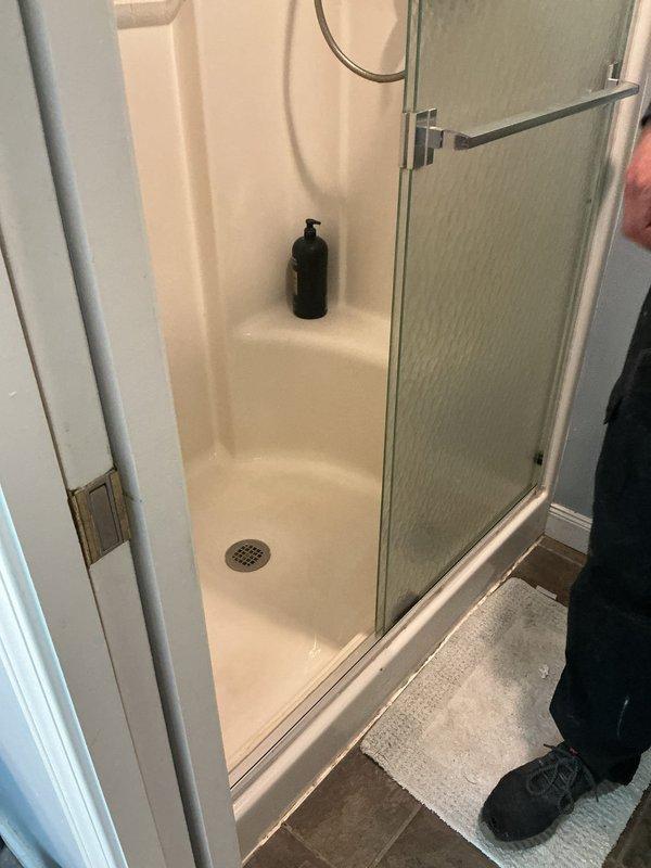 Responded to plumbing leak complaint originating from master bathroom shower causing water intrusion into flooring below. Conducted thorough inspection of shower stall, including white fiberglass enclosure, drain assembly, and surrounding components. Documented existing conditions with photographs showing shower pan configuration, built-in seating ledge, center drain with metal grid cover, and glass door assembly with chrome framing. Identified potential leak sources and assessed shower base integrity, wall sealing, and drain connections to determine cause of water migration into subfloor during shower operation.